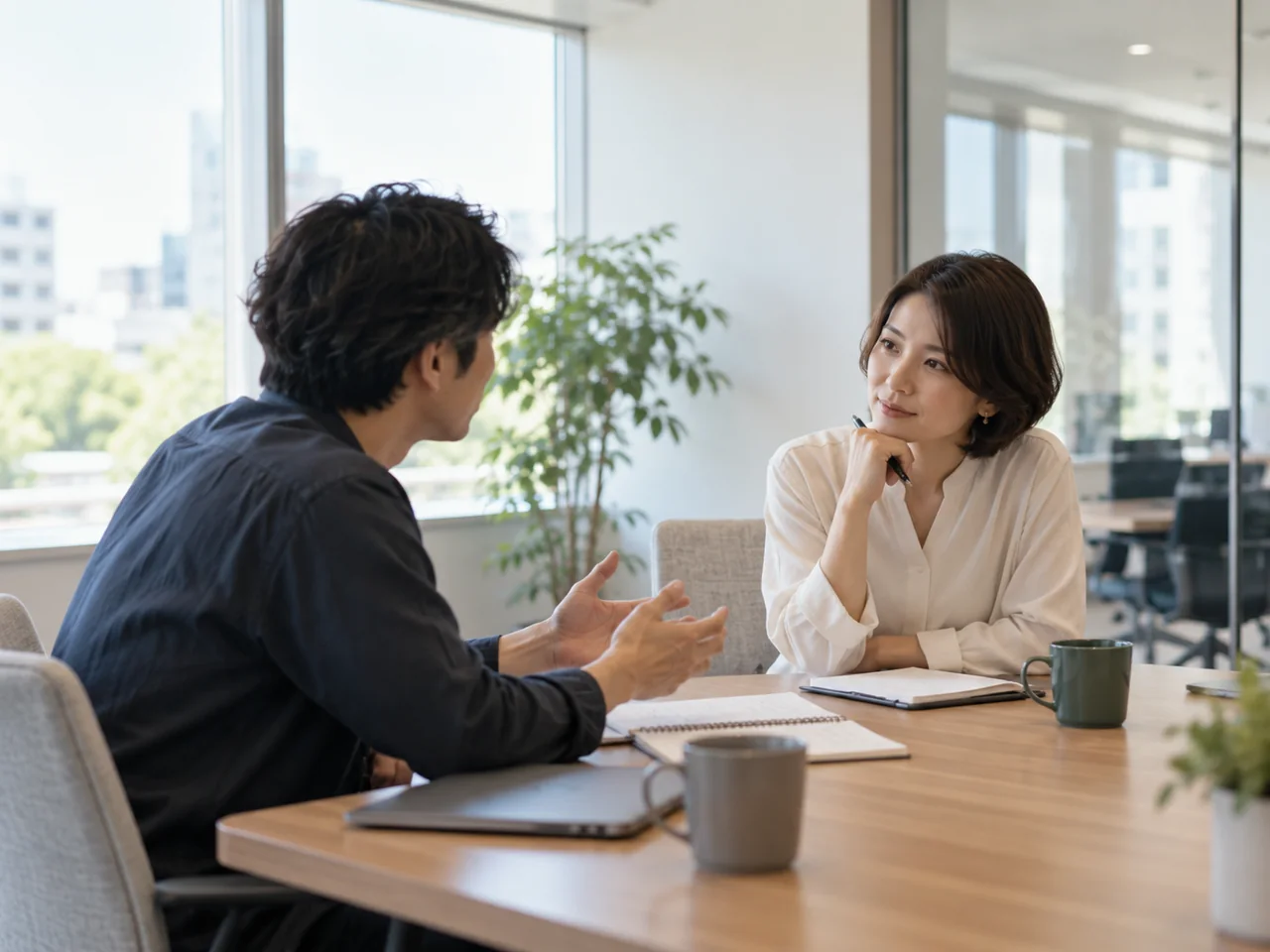 明るいオフィスのテーブルで話を聴き合う二人。生成イメージ