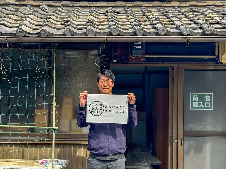 長屋の前で百人町百人衆プロジェクトの看板を持つメンバー